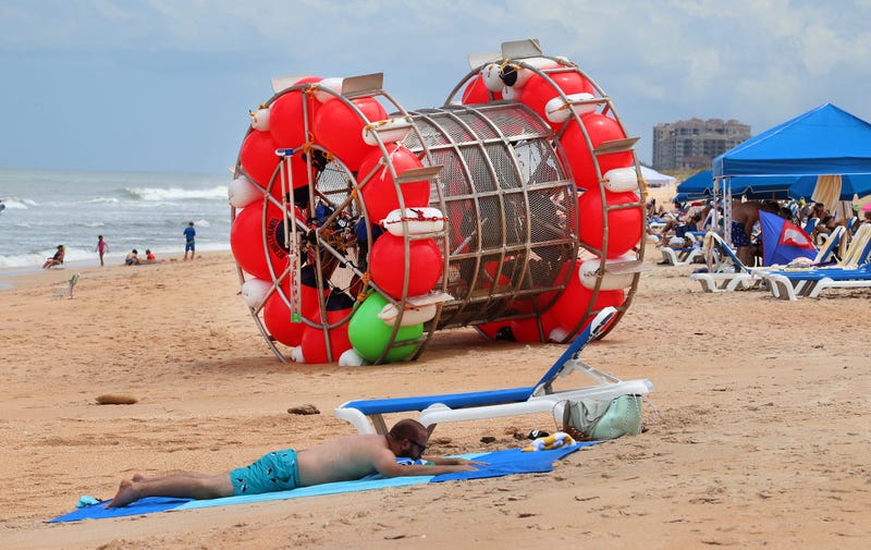 Beachgoers relax near a human-sized hamster wheel that came ashore in Daytona Beach, Florida, on July 26, 2021. The man aboard the vessel, Reza Ray Baluchi, was arrested in late August 2023 after he tried to ride across the Atlantic
