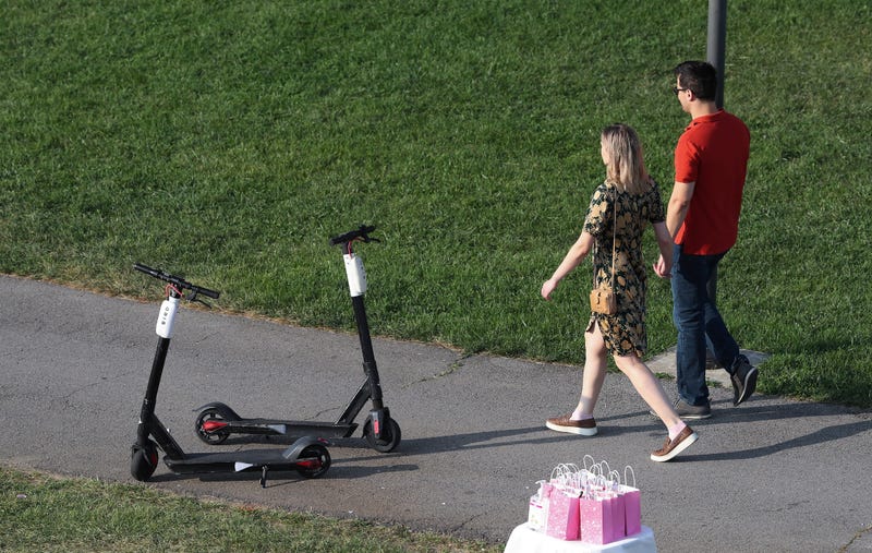 A couple walks past scooters left on the sidewalk at the Big Four Lawn in Louisville, Ky