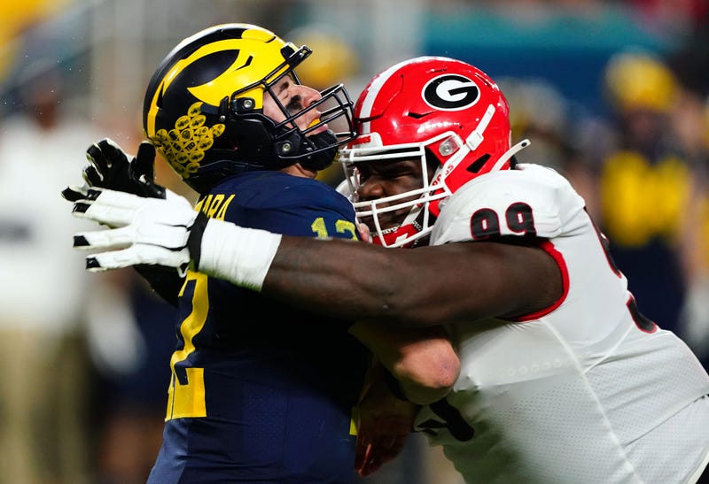 Dec 31, 2021; Miami Gardens, FL, USA; Michigan Wolverines quarterback Cade McNamara (12) is hit by Georgia Bulldogs defensive lineman Jordan Davis (99) during the third quarter in the Orange Bowl college football CFP national semifinal game at Hard Rock Stadium. 