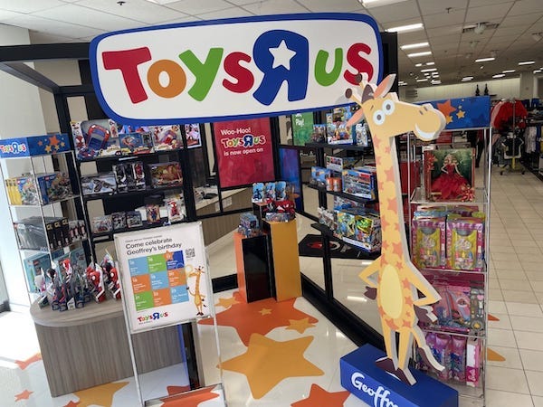 A Toys R Us display showing shelves of toys and Geoffrey the cartoon giraffe mascot greet visitors to Macy's in Augusta Mall, Oct. 19, 2022
