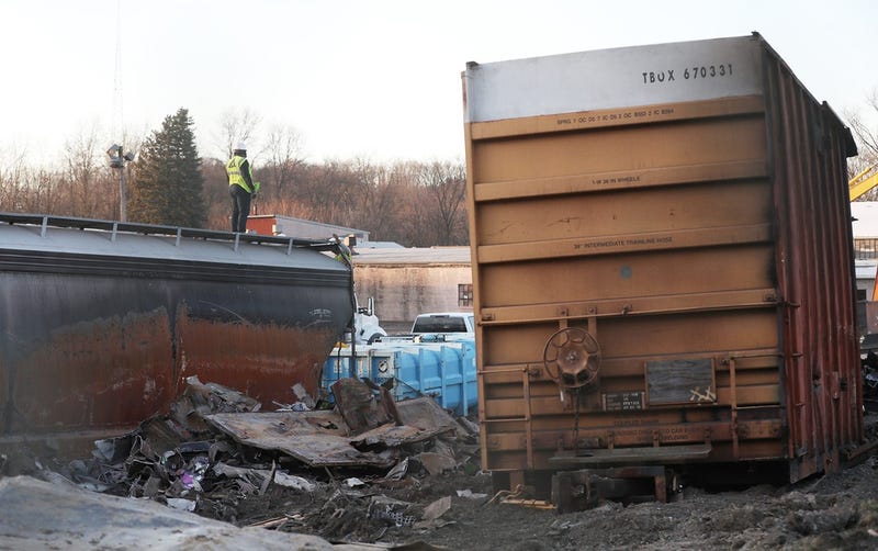 A worker stands on a tanker car next to a burnt out box car in a gated yard near the train tracks in East Palestine on Wednesday.