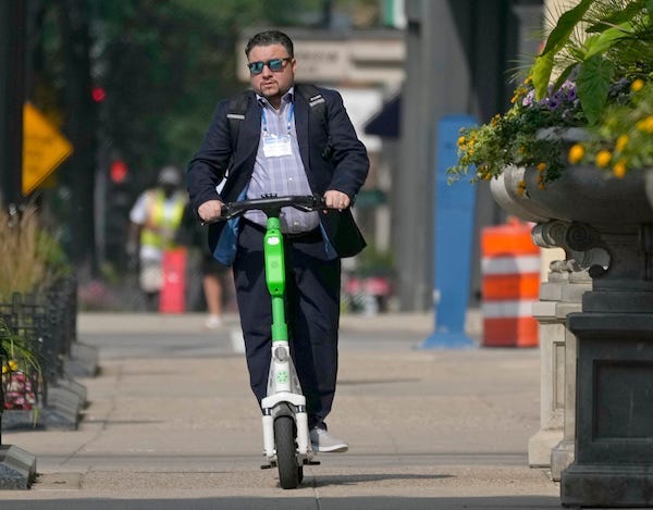 A man rides a Lime e-scooter on the sidewalk