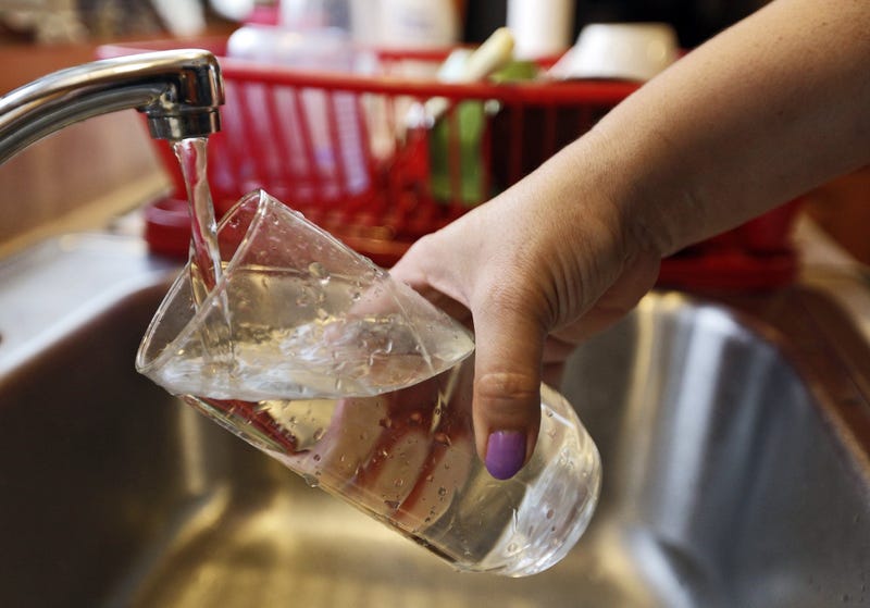 person fills glass of water from kitchen faucet 