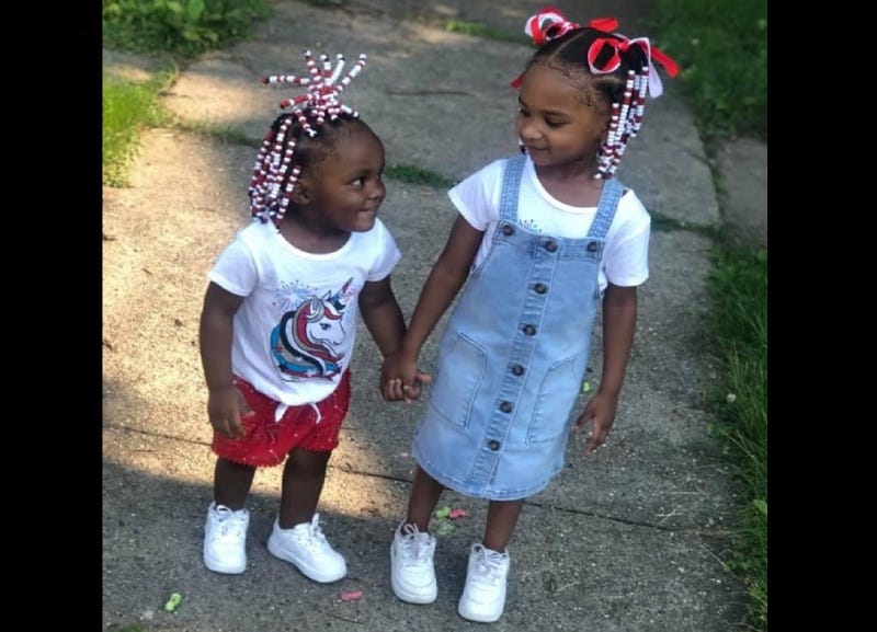 Two girls stand on a sidewalk.