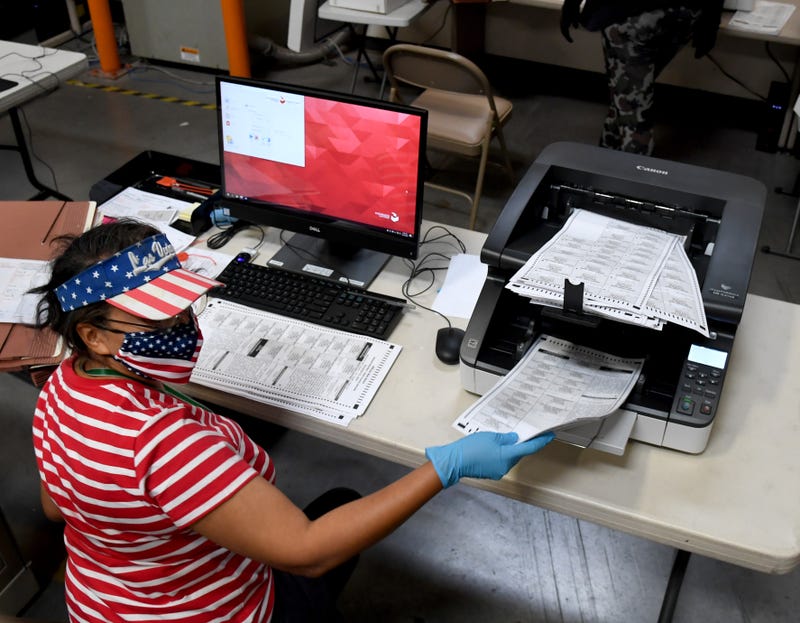 An election worker feeds mail-in ballots into a machine