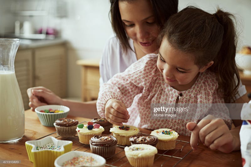 Little girl decorates cupcakes with help from her mom