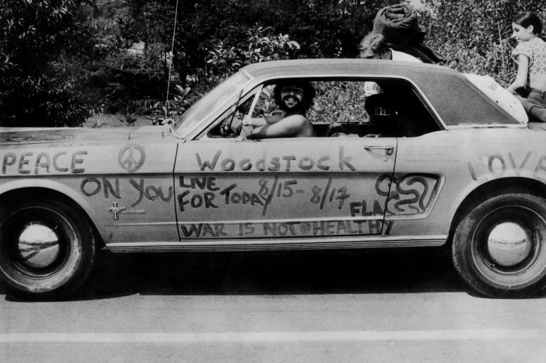 A music fan at Woodstock pop festival in his car covered in anti-war slogans for love and peace.