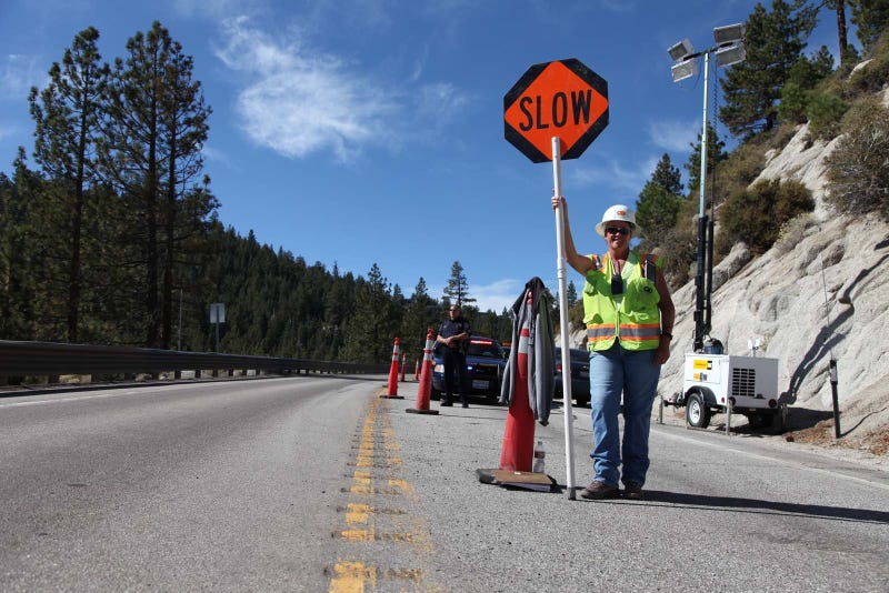 A road crew worker warns vehicles to slow down through a construction zone.