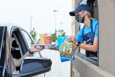 A worker delivering a Auntie Anne's bag and Jamba Juice to a customer via drive-through. 
