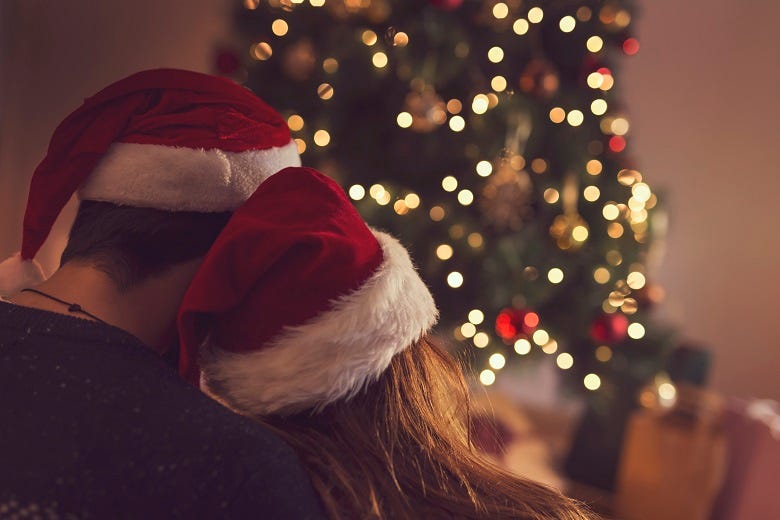 Couple with Santa hats sitting in front of Christmas tree