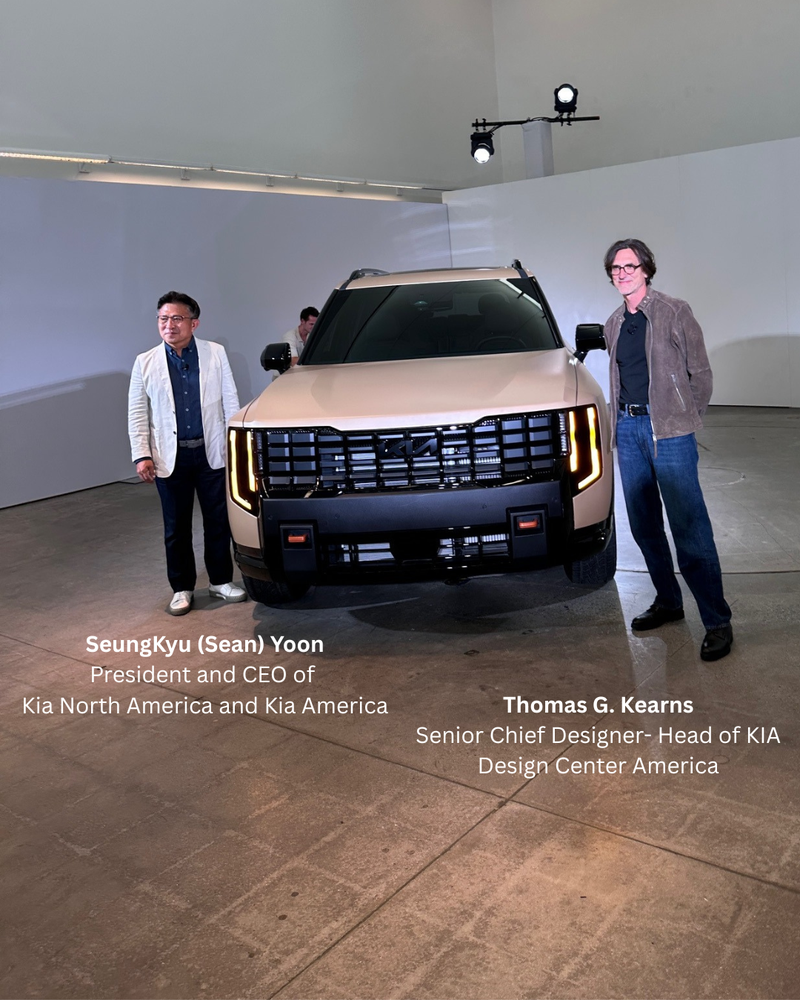 Two people stand beside a modern beige SUV in a spacious, well-lit showroom. The vehicle's design features bold vertical headlights, creating a sleek, futuristic look.