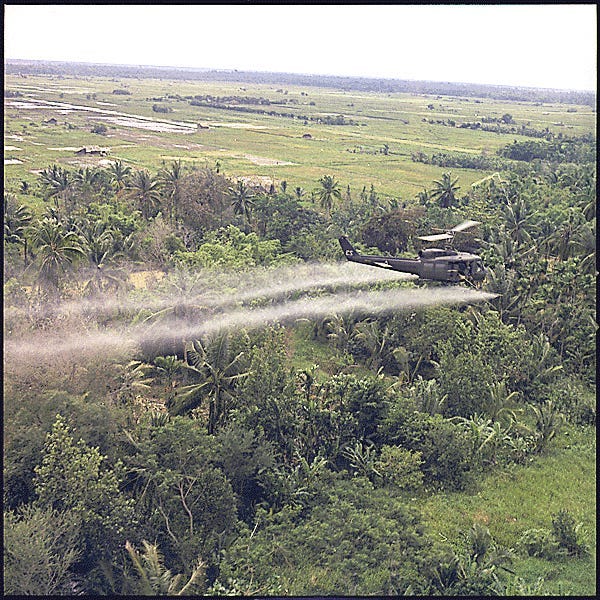 A helicopter sprays herbicide over jungle.