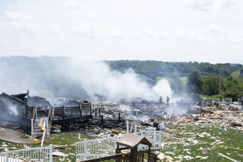 Two firefighters stand on the debris around the smoldering wreckage of the three houses that exploded in Plum, Pa., on Aug. 12, 2023. Three houses at the center of a recent explosion near Pittsburgh that killed six people will need to be torn down and 10 others are not currently inhabitable, county officials said over the weekend.