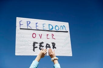 FILE - In this April 21, 2020, file photo a person holds a sign while gathering with others to protest stay-at-home orders put into place due to the COVID-19 outbreak outside the Missouri Capitol in Jefferson City, Mo. (AP Photo/Jeff Roberson, File)