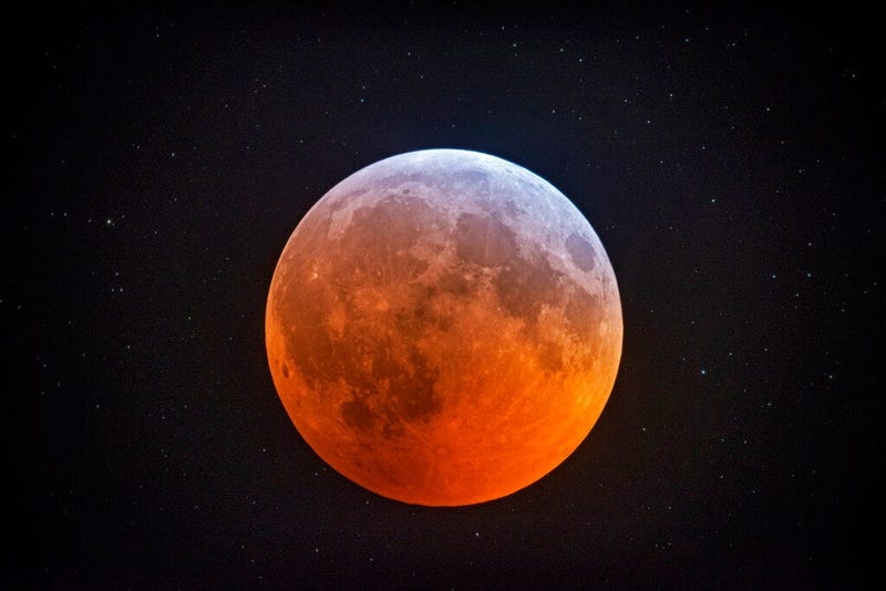 The totally eclipsed moon glows with a reddish color against the background stars