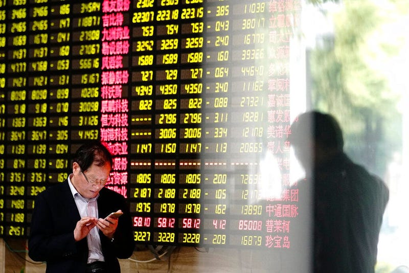 A man looks at his smartphone near a display showing stock prices at a brokerage house in Shanghai Monday, May 6, 2019. China's benchmark Shanghai Composite index dives on U.S. President Donald Trump threat of more China tariffs. At right is a reflection