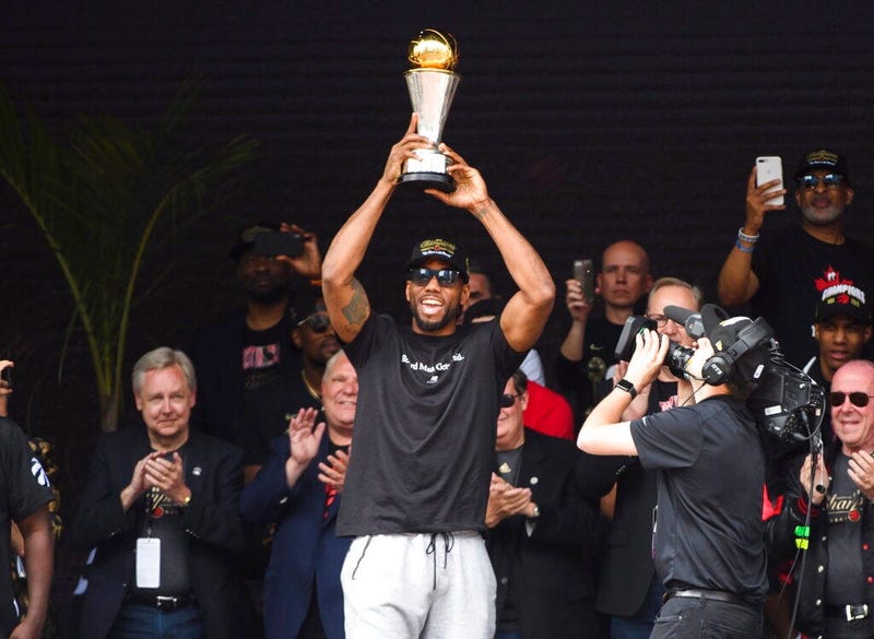 Toronto Raptors forward Kawhi Leonard hoists the MVP trophy next to teammates during the team's NBA basketball championship parade in Toronto, Monday, June 17, 2019.