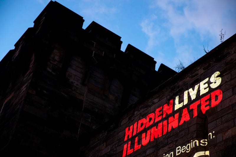 A new exhibit titled "Hidden Lives Illuminated" is projected on a wall of the Eastern State Penitentiary, a former prison that's now a museum.