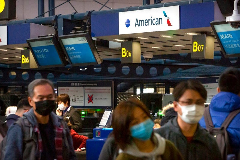 Travelers wearing face masks line up to check in for an American Airlines flight to Los Angeles at Beijing Capital International Airport in Beijing,