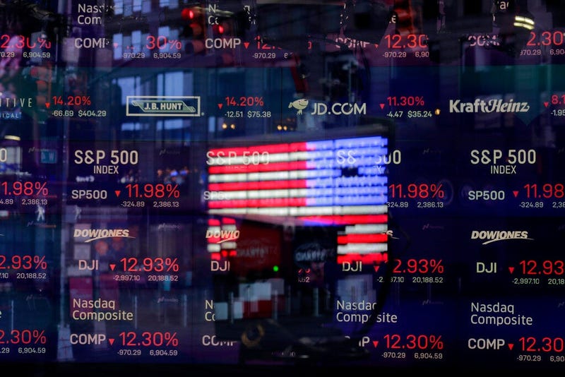 In this March 16, 2020 file photo, a United States flag is reflected in the window of the Nasdaq studio, which displays indices and stocks down, in Times Square, New York. (AP Photo/Seth Wenig, File)
