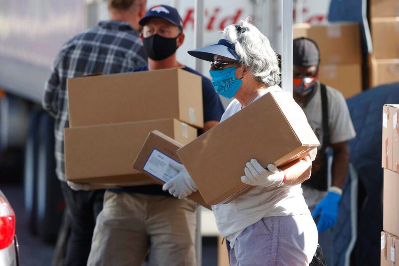FILE - In this June 26, 2020, file photo, volunteers Juanita MacKenzie, front, and Dave Stutman carry boxes of food to a waiting car at a large mobile pantry set up by the Food Bank of the Rockies. (AP Photo/David Zalubowski, File)