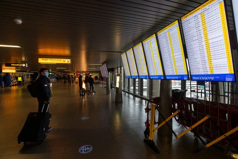 FILE- In this Friday Dec. 18, 2020, file photo, A traveller wearing a face mask checks the flight departures at Schiphol Airport, near Amsterdam, Netherlands.