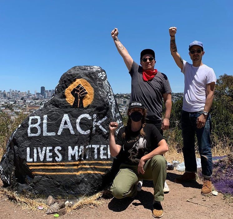 Artists Micah Rivera, Kseniya Makarova and Manny Fabregas in front of Bernal Heights rock that's painted "Black Lives Matter"