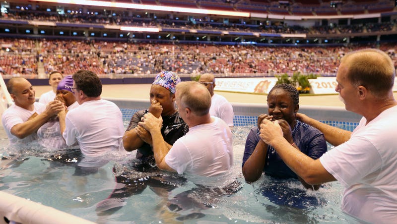 Three women wipe their faces after being batptized in a large swimming pool on the floor of the Dome at America’s Center in St. Louis on Saturday August 17, 2019