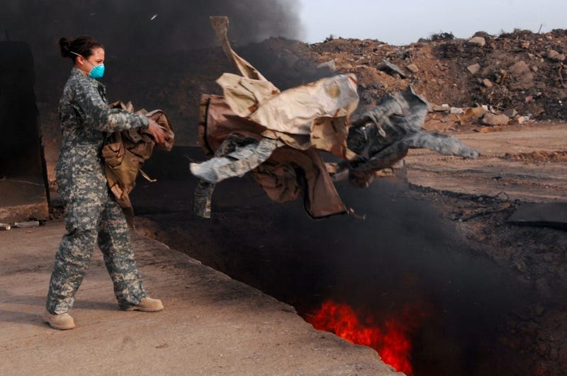 Senior Airman Frances Gavalis, 332nd Expeditionary Logistics Readiness Squadron equipment manager, tosses unserviceable uniform items into a burn pit, March 10.