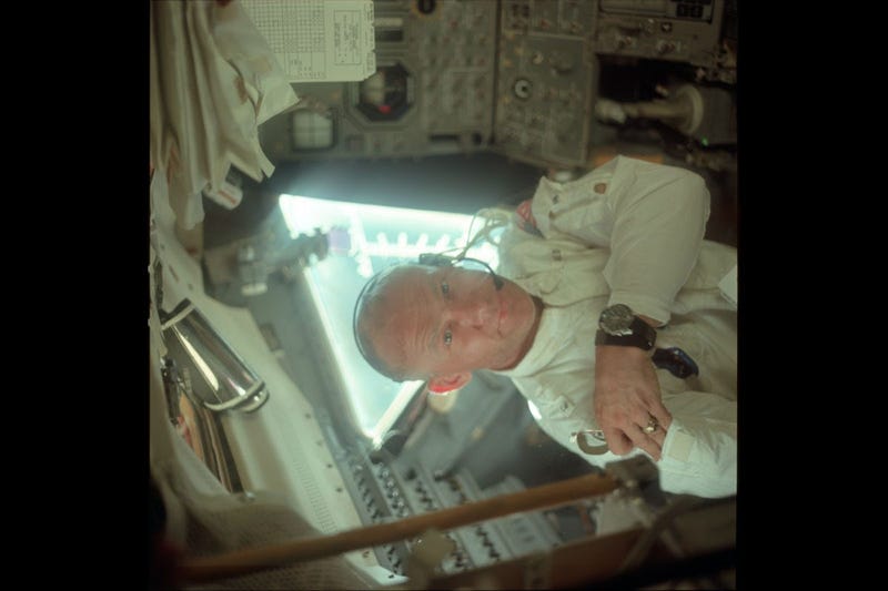 Buzz in the LM during its checkout en route to the Moon. He is on the left side of the cabin and is placing a pair of sunglasses in his jacket's arm pocket.