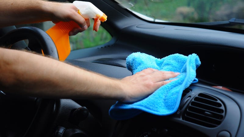 Hands wiping dashboard of a car with a cleaning cloth