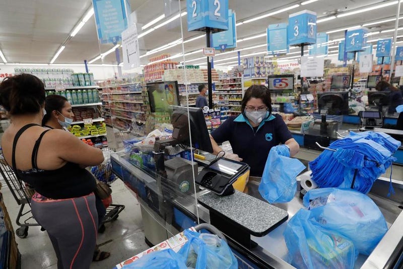 In this Wednesday, June 3, 2020 photo, cashier Rosario Vargas, center, bags groceries for customers at the Presidente Supermarket in the Little Havana neighborhood of Miami.