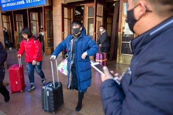 Travelers wear face masks as they walk outside of the Beijing Railway Station in Beijing, Monday, Jan. 20, 2020. China reported Monday a sharp rise in the number of people infected with a new coronavirus. (AP Photo/Mark Schiefelbein)