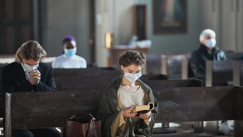 Young woman in protective mask sitting on bench and reading the Bible in the church