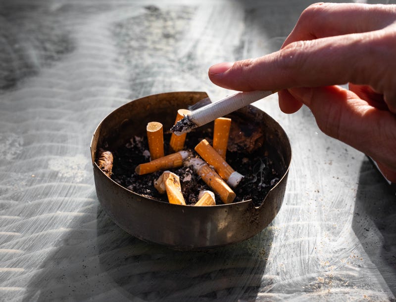 Person holding a cigarette whose ashes are tapped into an ashtray.