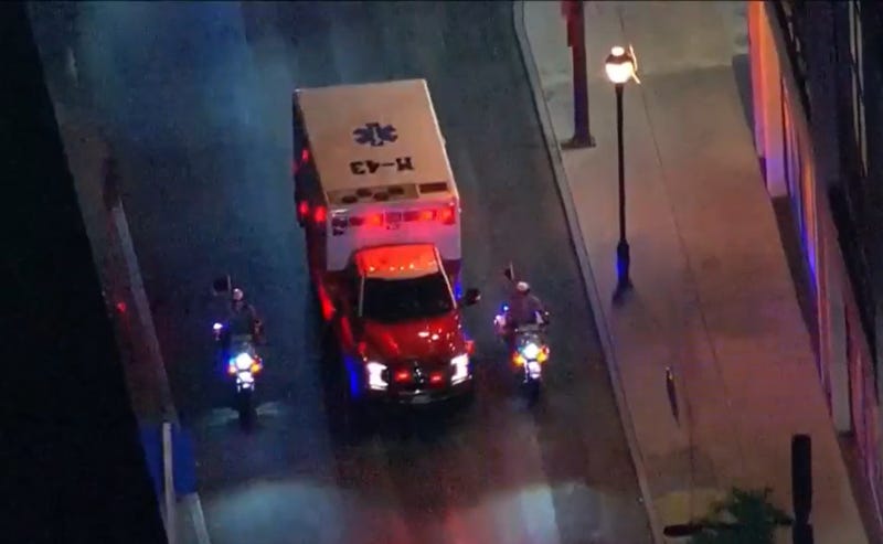 An ambulance is escorted by a pair of police officers on motorcycles.