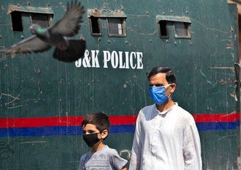 A Kashmiri man and a child wearing masks walk past a parked armored police vehicle in Srinagar, Indian controlled Kashmir, Monday, July 13, 2020. (AP Photo/Mukhtar Khan)