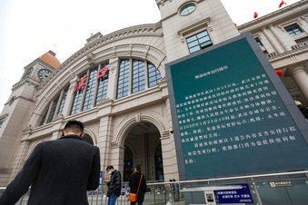 People walk past a billboard announcing the closure of the Hankou Railway Station in Wuhan in central China's Hubei Province, Thursday, Jan. 23, 2020. (Chinatopix via AP)