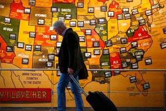 In this March 18, 2020 photo, a traveler checks his mobile telephone while passing a map of the United States on the way to the security checkpoint in the main terminal in Denver International Airport in Denver. (AP Photo/David Zalubowski)