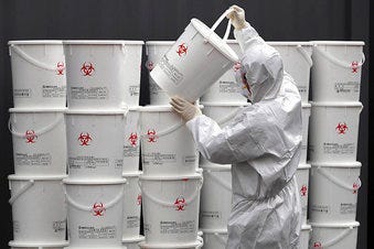 A worker in protective gear stacks plastic buckets containing medical waste from coronavirus patients at a medical center in Daegu, South Korea, Monday, Feb. 24, 2020. (Lee Moo-ryul/Newsis via AP)