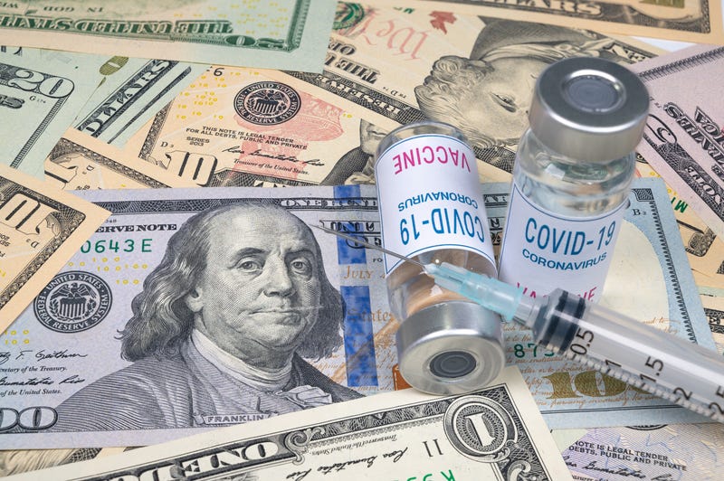 Syringes and COVID-19 vaccine ampoule lying on top of US currency