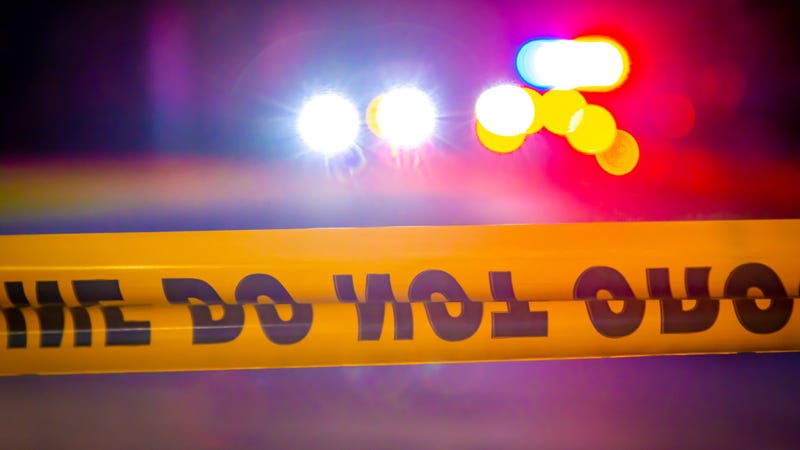 Generic and blurry police lights from a cruiser vehicle and car headlights behind yellow crime scene do not cross caution tape at night.