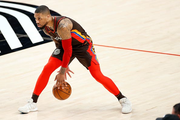 Damian Lillard dribbles between his legs. 