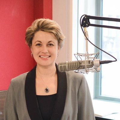 Debbie MOnterrey stands in front of a microphone. she is a white woman with short blond hair and a gray jacket