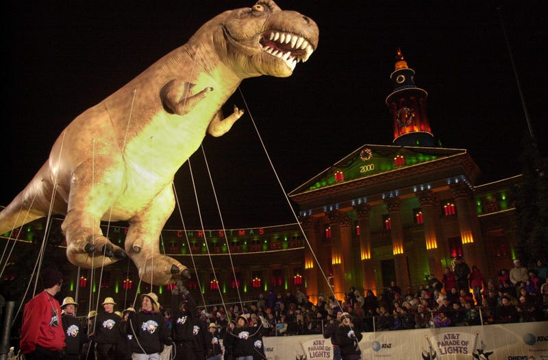 A T-Rex balloon parade balloon floats over handlers in front of the Denver City Council building decorated for the holidays
