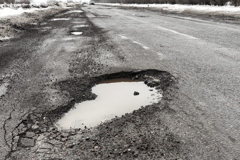 Old highway with holes and snow. Landscape road in the potholes in cloudy winter weather. The concept of the absence of timely repair of the highway.