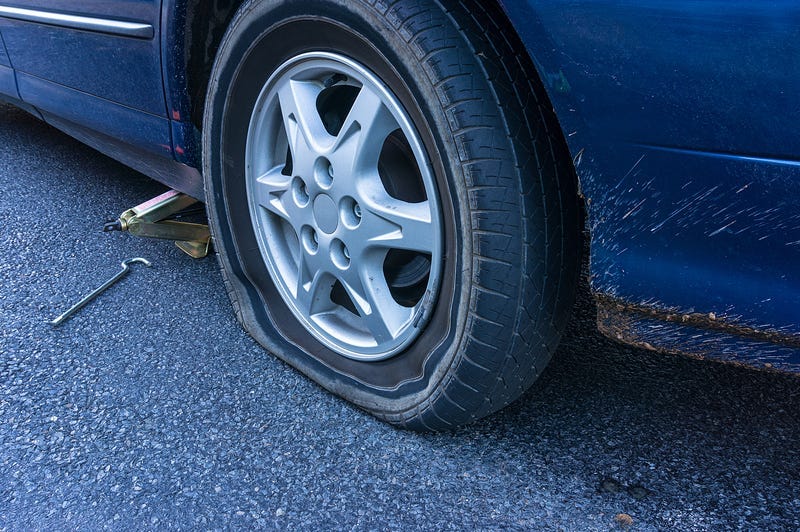 Blue car with flat tire on the road.