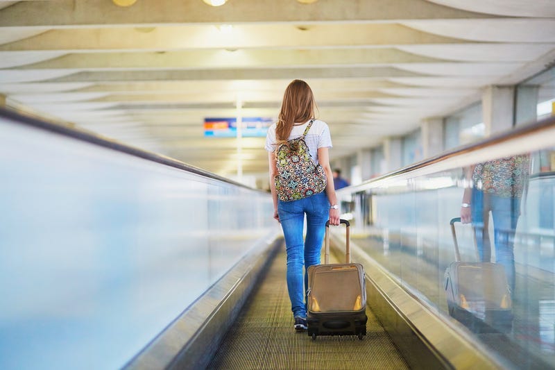 Tourist girl with backpack and carry on luggage in international airport, on travelator