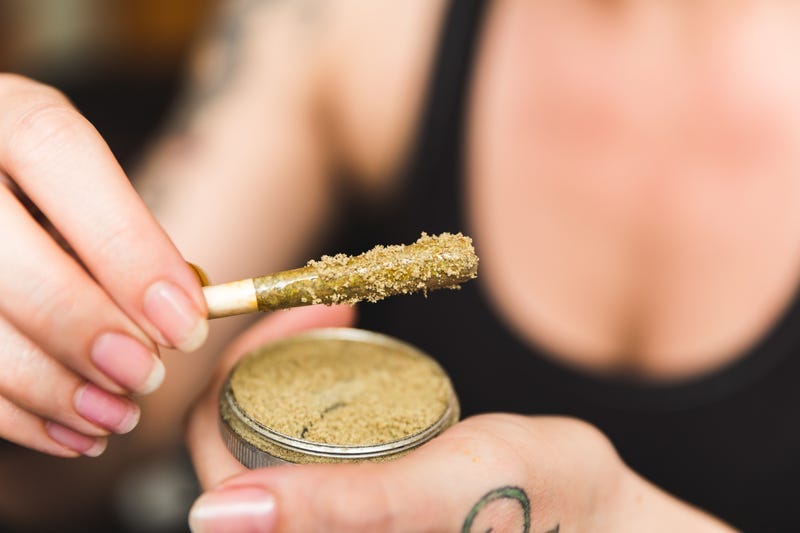 Woman holding a cannabis or marijuana joint in her hand. Joint is dipped in oil or wax and sprinkled with kief