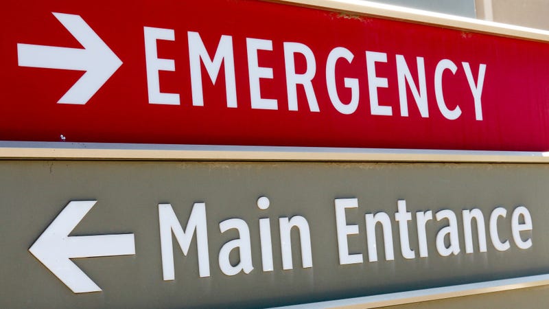 Tilted, full frame image of a gray and red sign at a hospital that says the emergency room is to the right and the main entrance is to the left